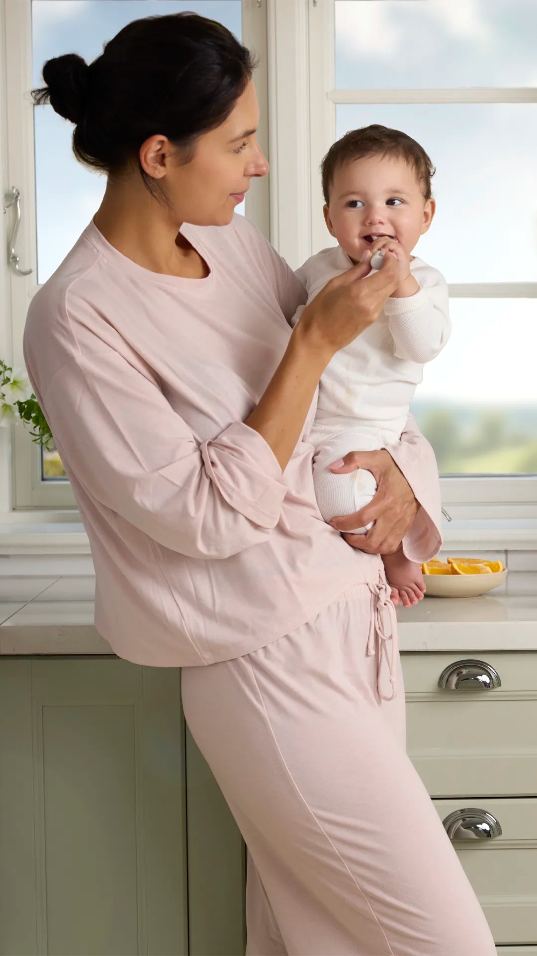 Eine Mutter in der Küche gibt ihrem Kleinkind einen Löffel, während ein älteres Mädchen daneben sitzt; BiGaia Produkte stehen auf der Arbeitsplatte.