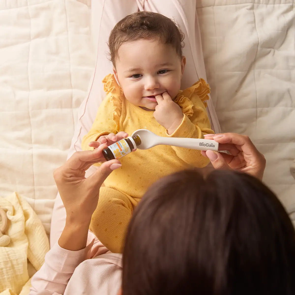 Eine Mutter gibt vorsichtig BiGaia Protectis Baby-Tropfen auf einen Löffel für ihr Baby, das auf ihrem Schoß liegt.