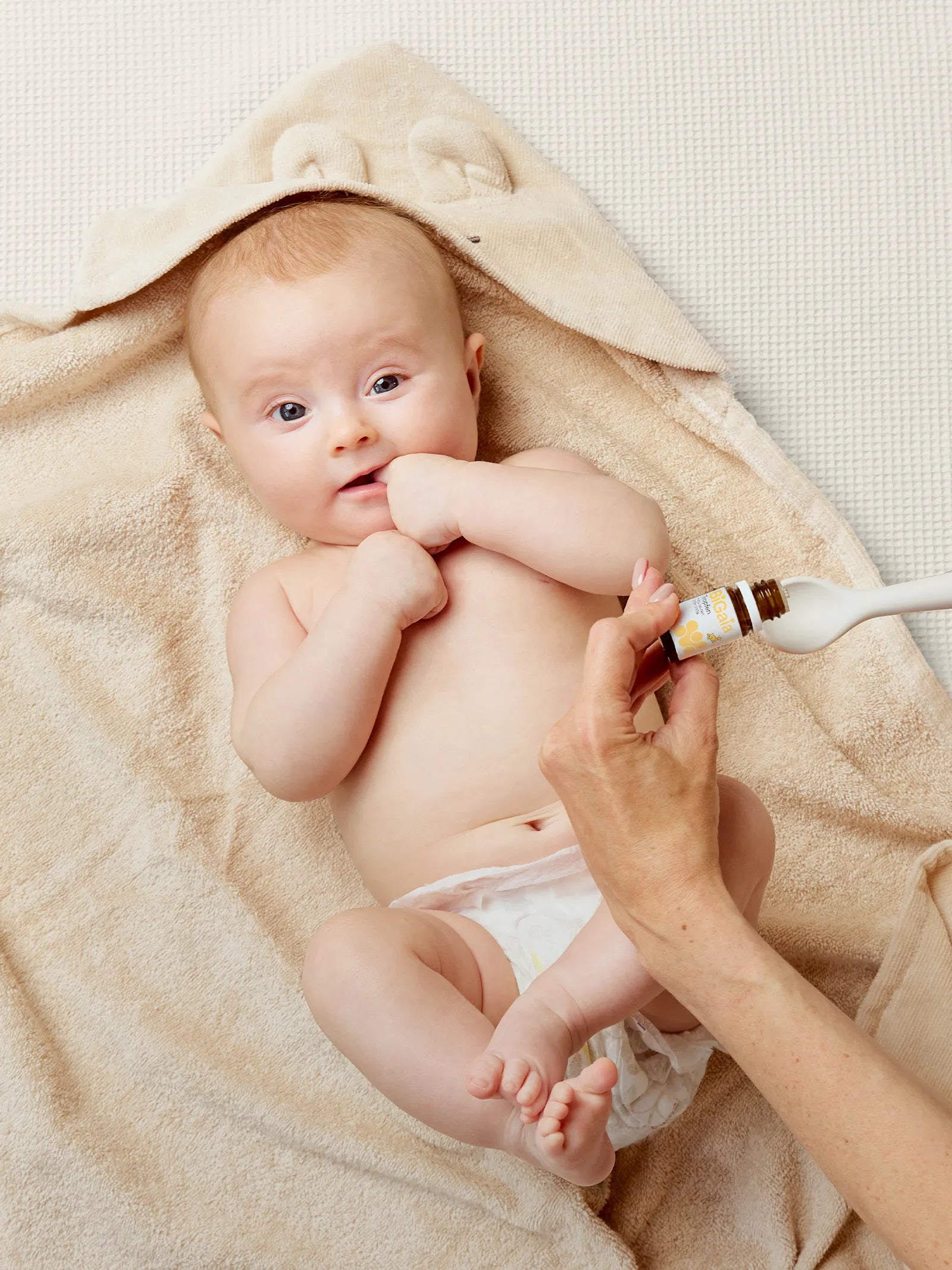 Ein Baby liegt nach dem Baden auf einem Handtuch, während ein Elternteil die BiGaia Tropfen auf einen Löffel gibt.