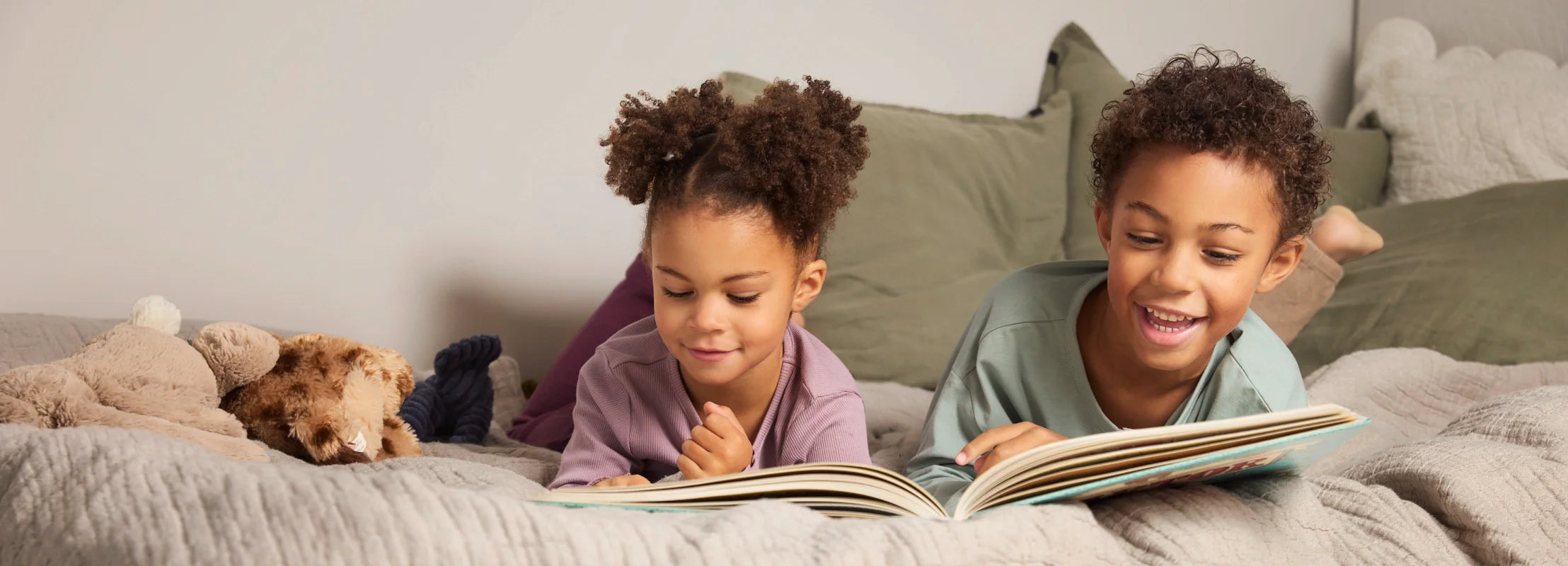 Zwei Kinder liegen gemütlich auf einem Bett und lesen gemeinsam mit Begeisterung in einem Bilderbuch.