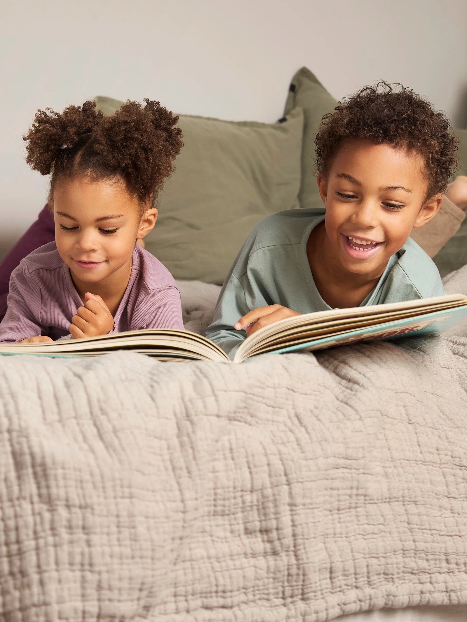 Zwei Kinder liegen gemütlich auf einem Bett und lesen gemeinsam mit Begeisterung in einem Bilderbuch.