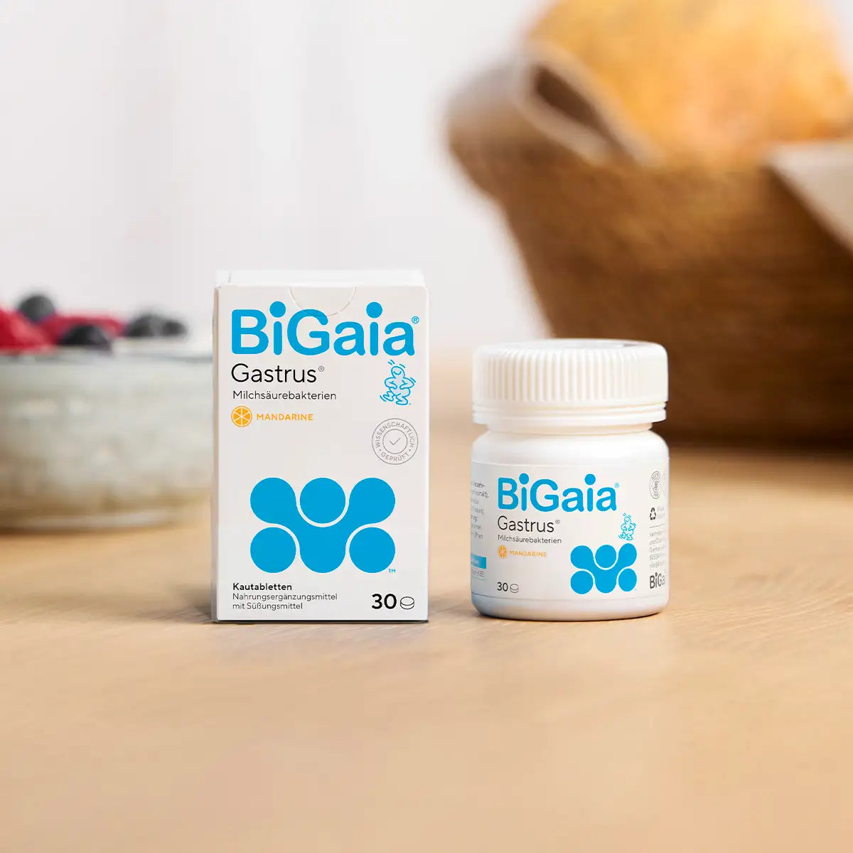 BiGaia Gastrus Packung und Dose auf einem Holztisch neben einer Schale mit Beeren und einem Brotkorb.