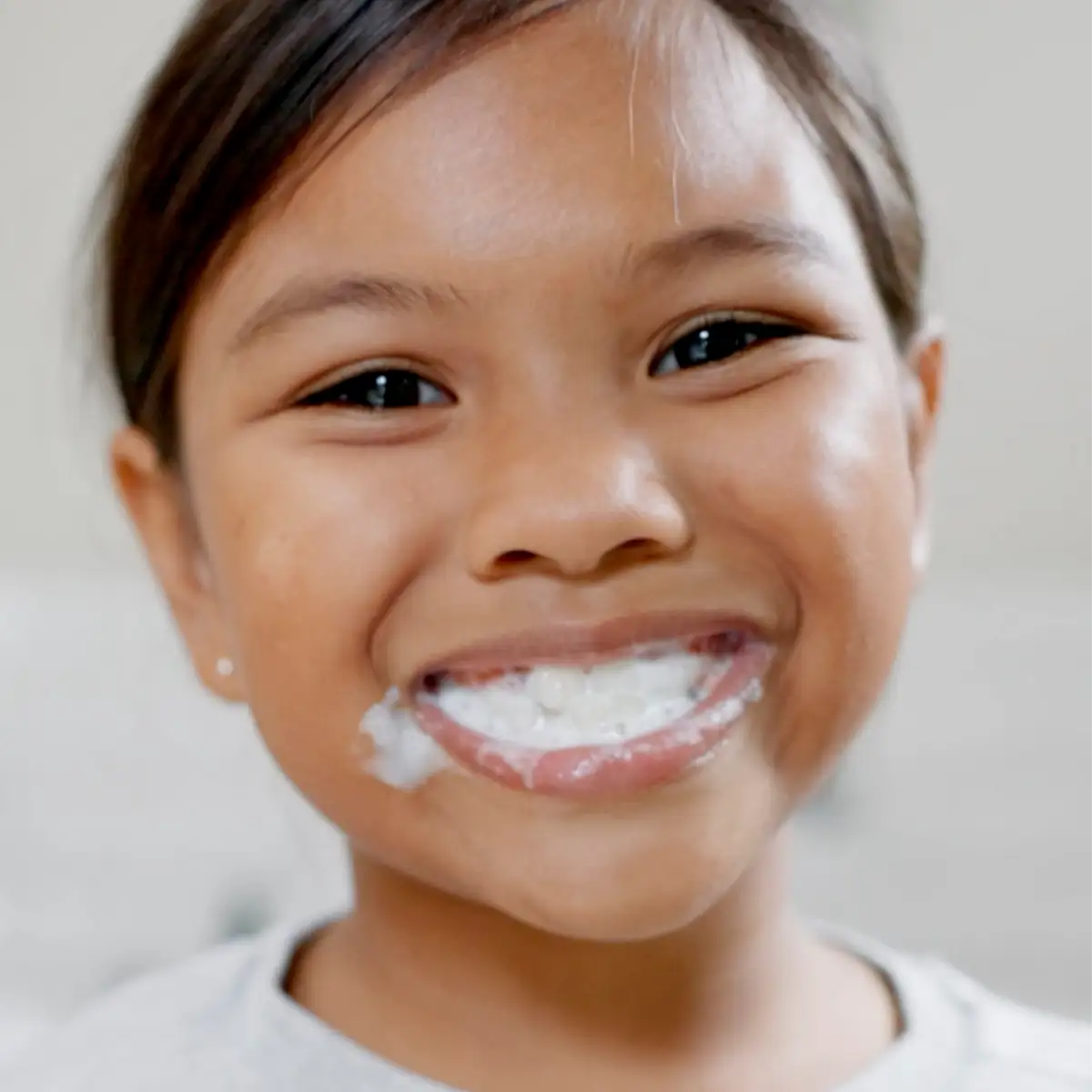 Nahaufnahme eines lächelnden Kindes beim Zähneputzen mit weißem Zahnpastaschaum im Mund.